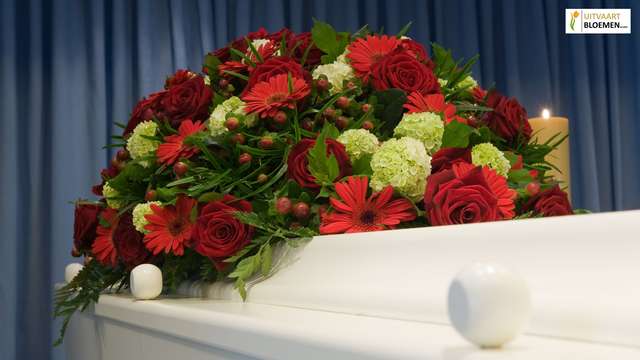 Rood rouwstuk met rozen en lelies op een kist tijdens een uitvaartceremonie.